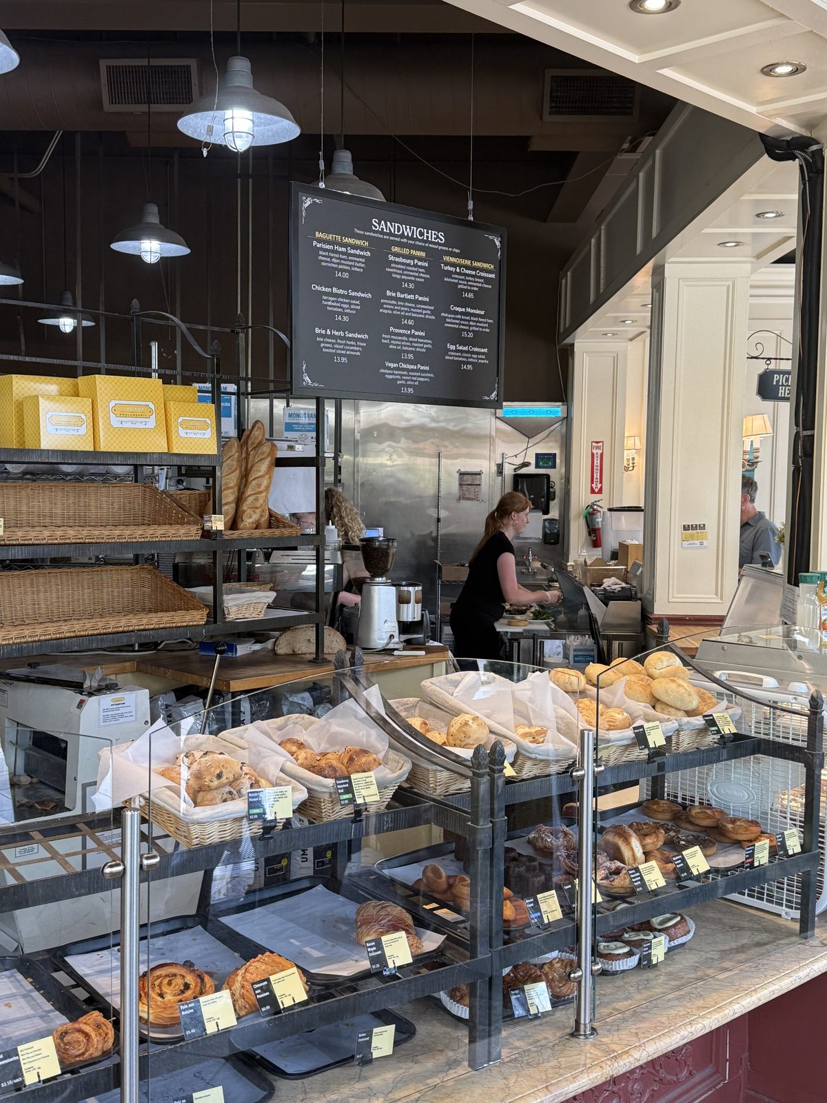 The case at the counter — baguettes, viennoiserie, and the sandwich board overhead. Everything in this photo is made in the building.