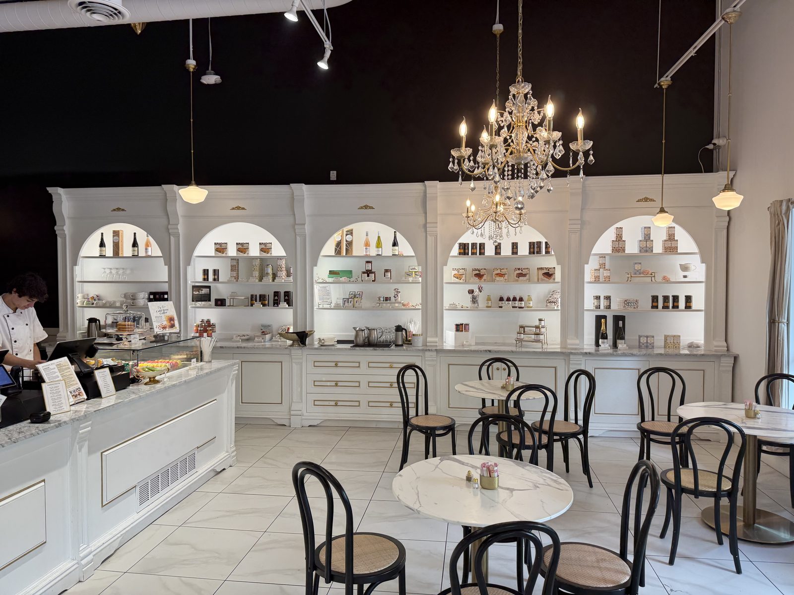 Inside — white marble, gold trim, a chandelier over four small tables. The whole room is styled like the pastries in the case.